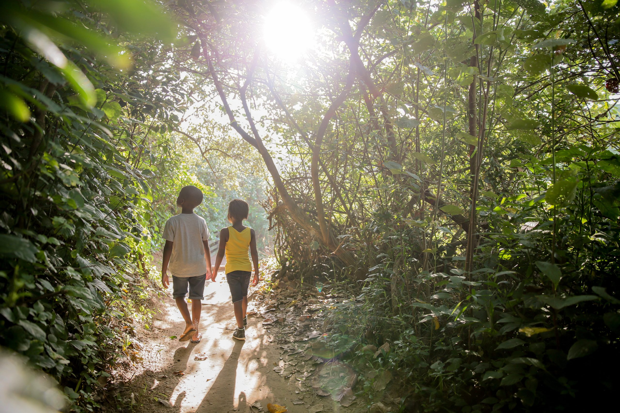 two kids walking in a forest near a beach 